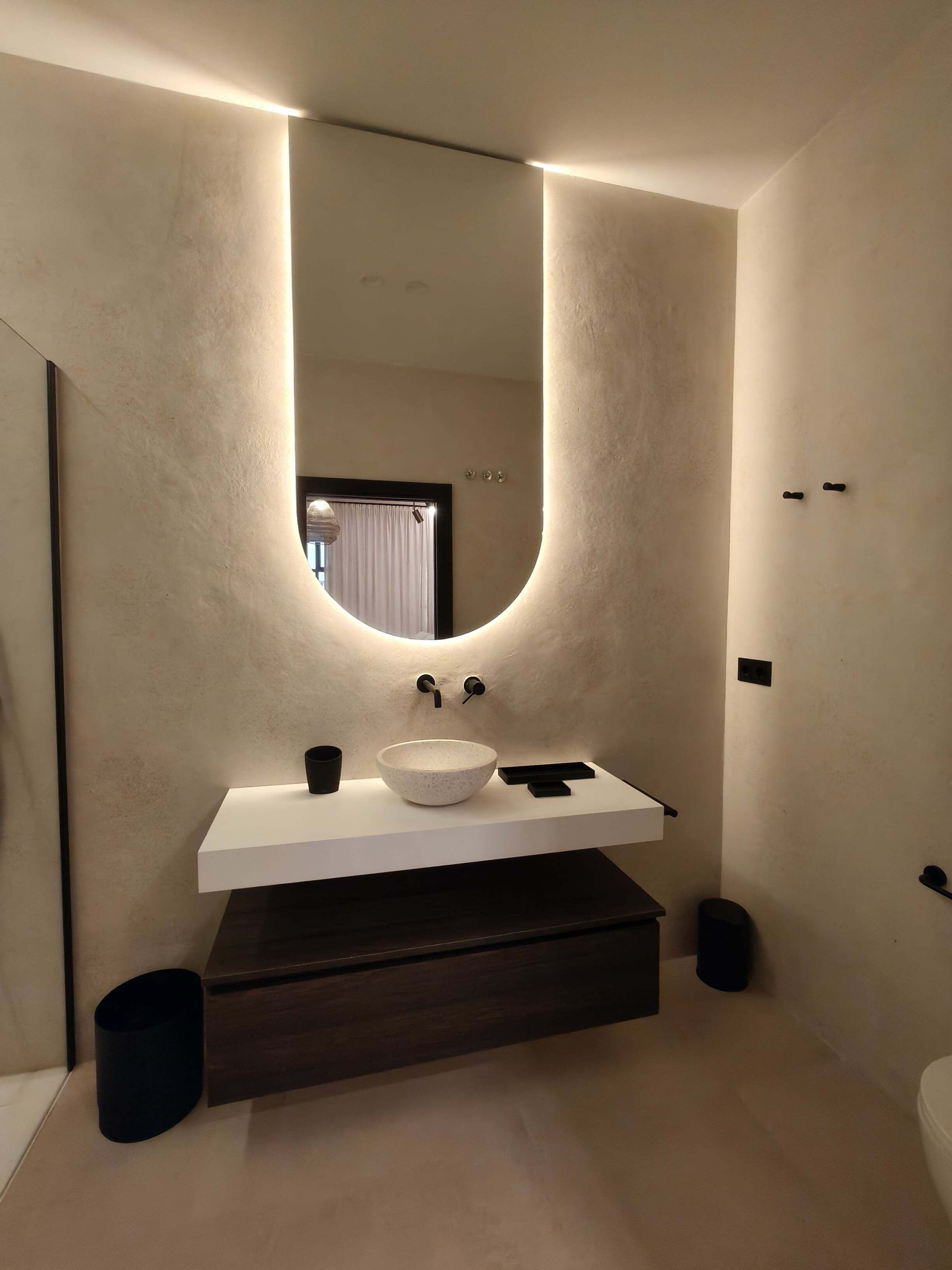 A modern bathroom with a large mirror, a white sink, and a dark wooden vanity.