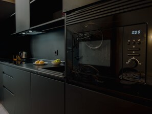 Uma cozinha moderna com micro-ondas embutido, chaleira e uma tigela de frutas na bancada.