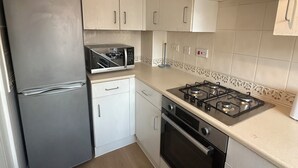 Cozinha compacta com geladeira, micro-ondas, fogão, forno e armários brancos.