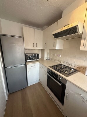A compact kitchen with a refrigerator, microwave, stove, oven, and white cabinets. - 2-Bed Home with Parking, Near Birmingham Airport, NEC & JLR (Birmingham)