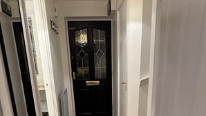Um corredor com piso de madeira, uma porta preta com painel de vidro e um tapete de boas-vindas.
