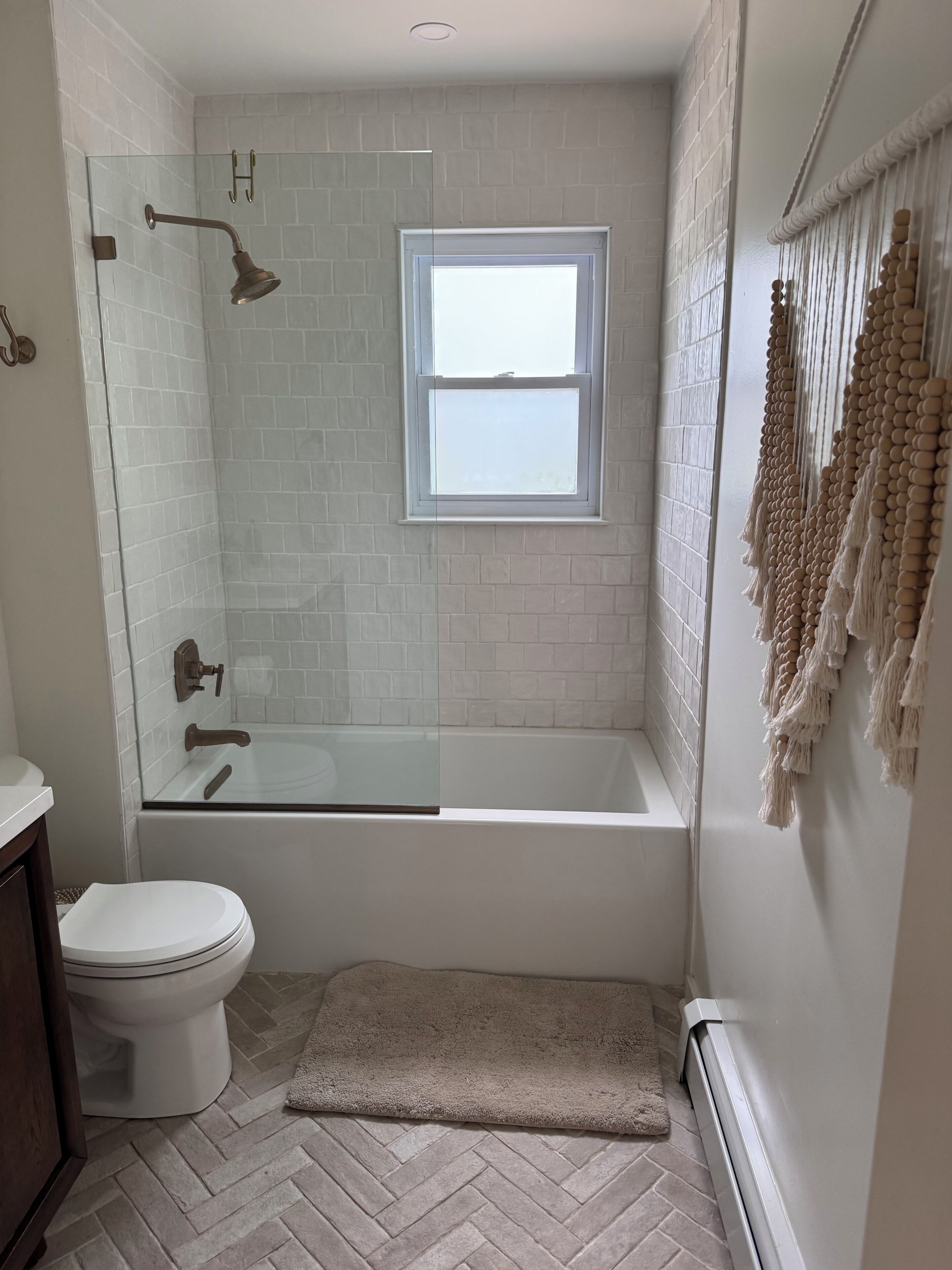 Un baño con ducha de vidrio, bañera blanca, inodoro y ventana.