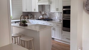 A modern kitchen with white cabinetry, a central island with stools, a built-in oven, and a herringbone-patterned backsplash. - Beautiful 3-bedroom house minutes from Swarthmore! (Morton)