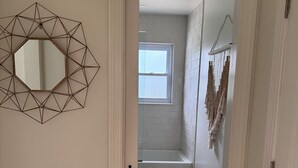 A hallway leading to a bathroom with a geometric mirror, a window, and a towel rack. - Beautiful 3-bedroom house minutes from Swarthmore! (Morton)