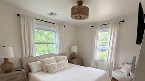 A bedroom with a large bed, two bedside tables, a chair, and a ceiling light fixture. - Beautiful 3-bedroom house minutes from Swarthmore! (Morton)