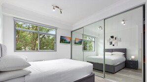 Une chambre moderne avec un grand lit, une cloison en verre et des œuvres d’art accrochées aux murs.