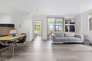 Een moderne woonkamer met een grijze bank, een eettafel met stoelen en een keuken met witte kasten.