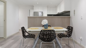 Un espace repas moderne avec une table blanche, des chaises noires et un vase rempli de fleurs blanches.
