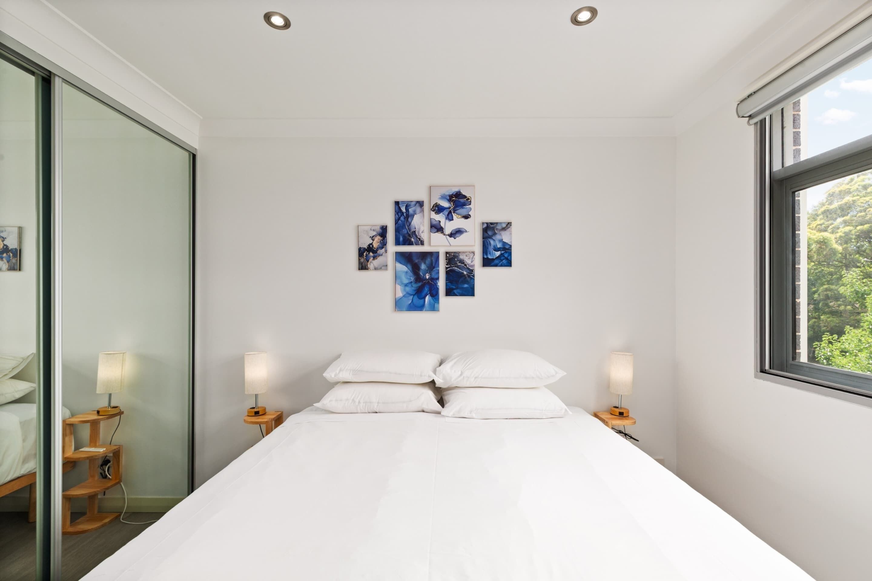 A modern hotel room with a large bed, bedside lamps, and a wall-mounted artwork.
