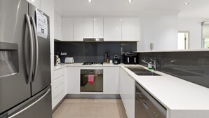 Une cuisine moderne dotée d’appareils électroménagers en acier inoxydable, de meubles blancs et d’un four encastré.