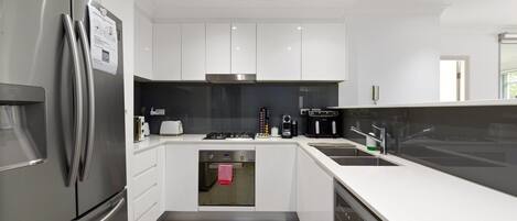 A modern kitchen with stainless steel appliances, white cabinetry, and a built-in oven.
