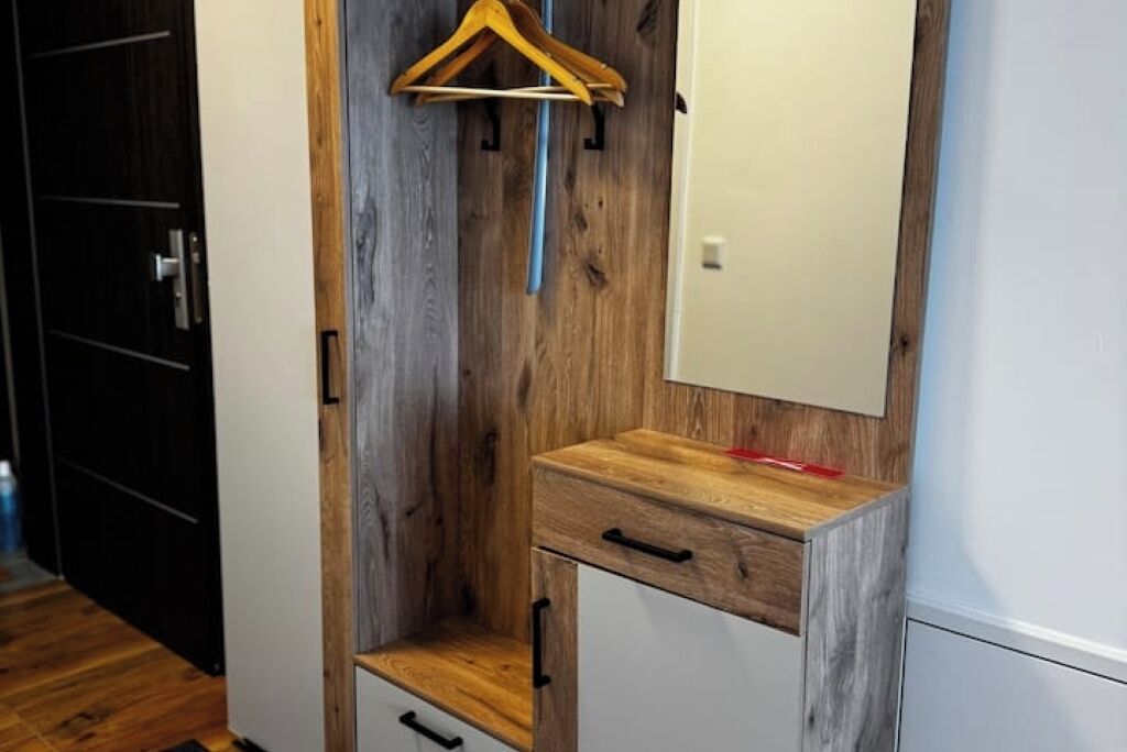 Quarto com parede de destaque em madeira, um armário branco com gavetas e um cabide de madeira na parede.