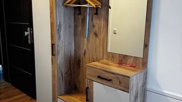 Quarto com parede de destaque em madeira, um armário branco com gavetas e um cabide de madeira na parede.