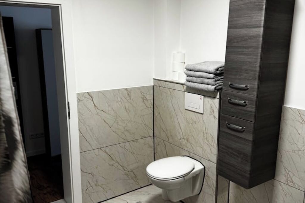 Een badkamer met toilet, een handdoekrek met handdoeken en een donker houten kastje.