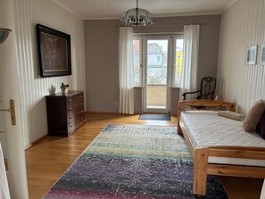 Una habitación con cama, cómoda, silla, mesa y ventana con cortinas.