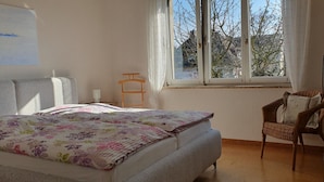 Ein Schlafzimmer mit einem Bett, einem Sessel, einem Fenster und einem Bild an der Wand.