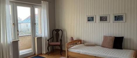 A bedroom with a bed, a chair, a hanging light fixture, and a view through a window.