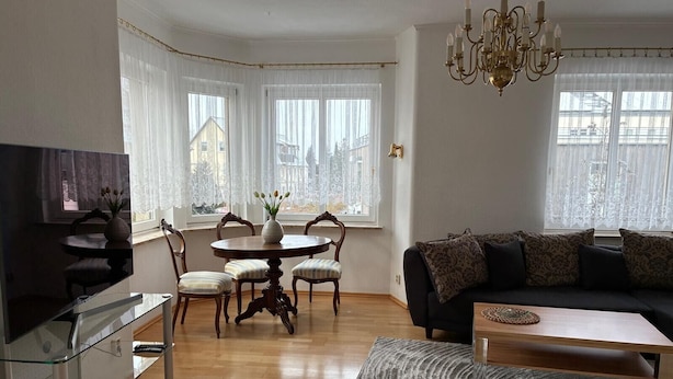 Ein Wohnzimmer mit Fernseher, Esstisch, Stühlen, einer Couch und einer Deckenleuchte.