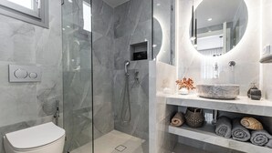 Une salle de bain moderne avec une douche à parois de verre, des toilettes, un meuble-lavabo avec un miroir rond et des serviettes soigneusement pliées.