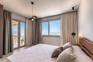 A bedroom with a large bed, a view of the city, and a balcony.