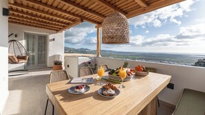 Een terras met een houten tafel gedekt voor het ontbijt, een hanglamp van riet en uitzicht op het landschap.
