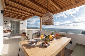 A terrace with a wooden table set for breakfast, a wicker hanging light, and a view of the landscape. - Eartha Horizon 3BR Villa Private Pool Scenic View (Naxos)
