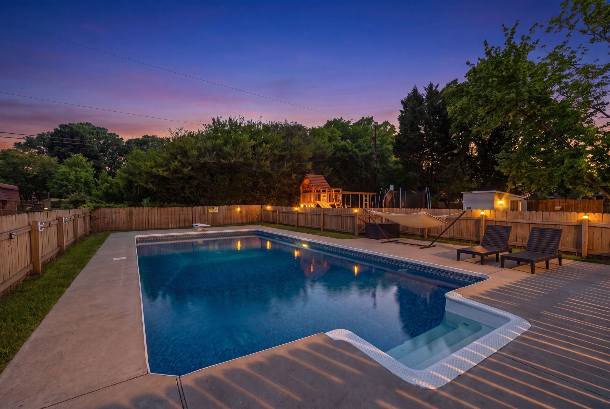 Una piscina rectangular con un deck alrededor, una cerca de madera y un deck con sillas de descanso.