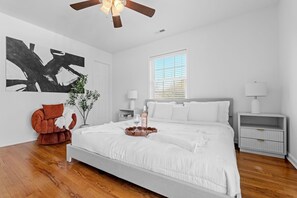 A bedroom with a large bed, a ceiling fan, a window with blinds, a bedside table with a lamp, and a wall-mounted abstract art piece. - Private Pool-4BR- 2.5 BT- 12min Clemson Univ (Pendleton)