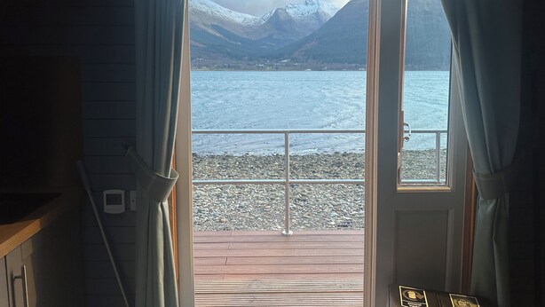 Ein Zimmer mit Blick auf einen See und Berge, durch eine offene Tür hindurch.