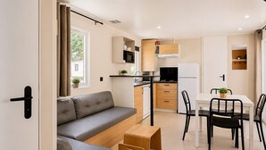 Ein kompakter Wohnbereich mit Sofa, Esstisch, Stühlen, einer Küchenzeile und einem kleinen Fenster.