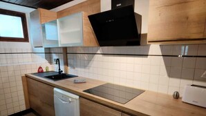 Une cuisine avec des meubles de rangement en bois, une hotte noire, un lave-vaisselle et un pare-feu en carrelage.