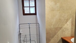 Une petite salle de bain avec un étendoir à linge en métal, une petite fenêtre, un lavabo et une poubelle.