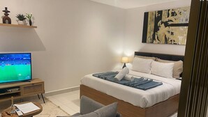 A modern bedroom with a bed, a TV, a bedside table, a lamp, and a wall art piece. - Unique Abodes (Accra)