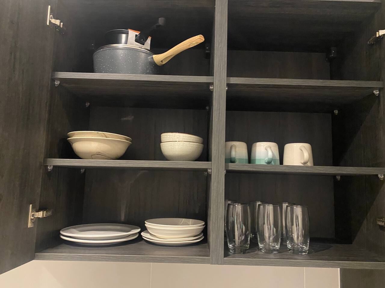 A kitchen cabinet with shelves holding various kitchenware including bowls, plates, glasses, and a kettle.