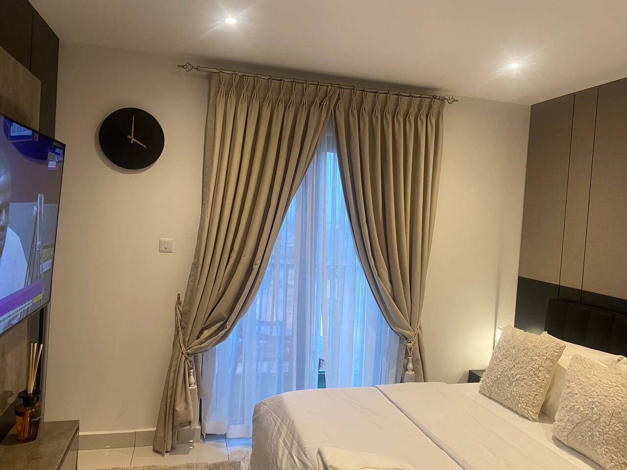 A modern bedroom with a large bed, a TV on the left, and a window with curtains.