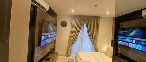 A modern hotel room with a bed, a desk, a chair, a TV, and an air conditioning unit.