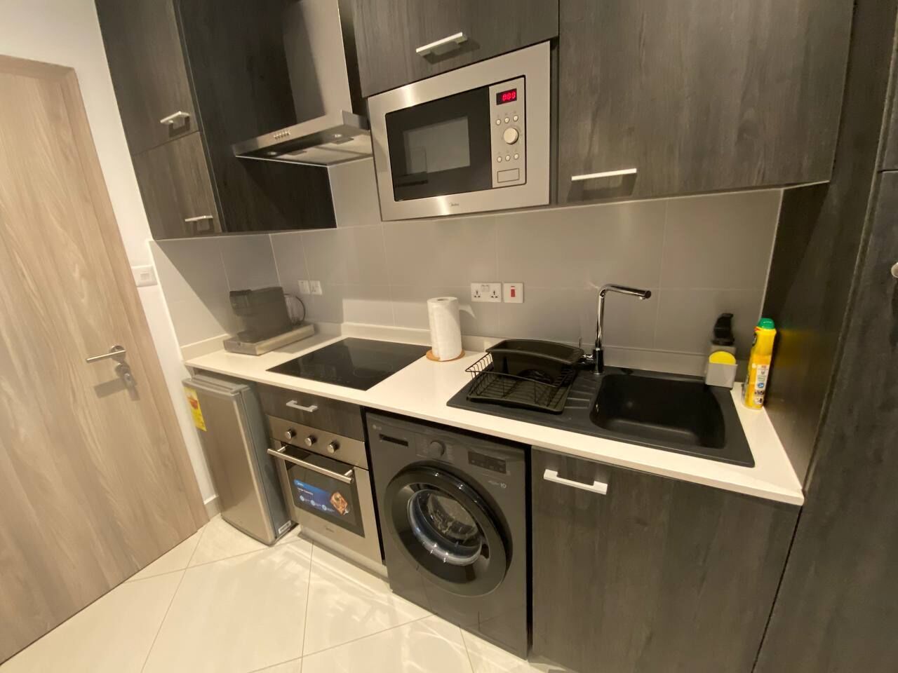 Een kleine keuken met een magnetron, wastafel en wasmachine.