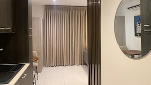 A modern kitchen with dark cabinetry, a dining area with a table and chairs, and a large window with curtains. - Unique Abodes (Accra)