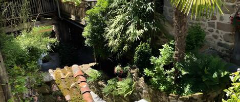 Un edificio de piedra con techo de tejas, rodeado de abundante vegetación y plantas en macetas.