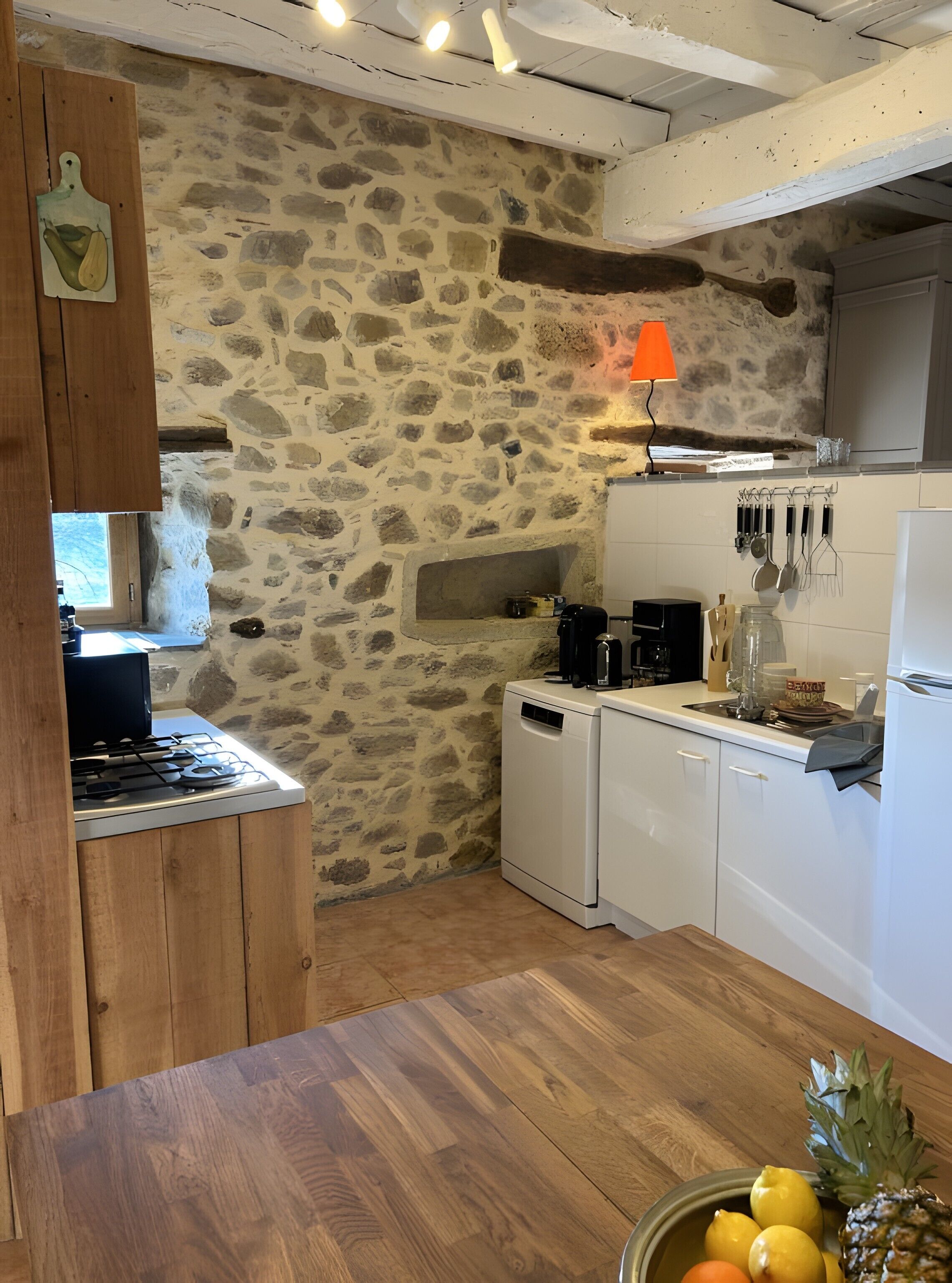 A kitchen with stone walls, a wooden cabinet, a stove, a dishwasher, and a fruit bowl.
