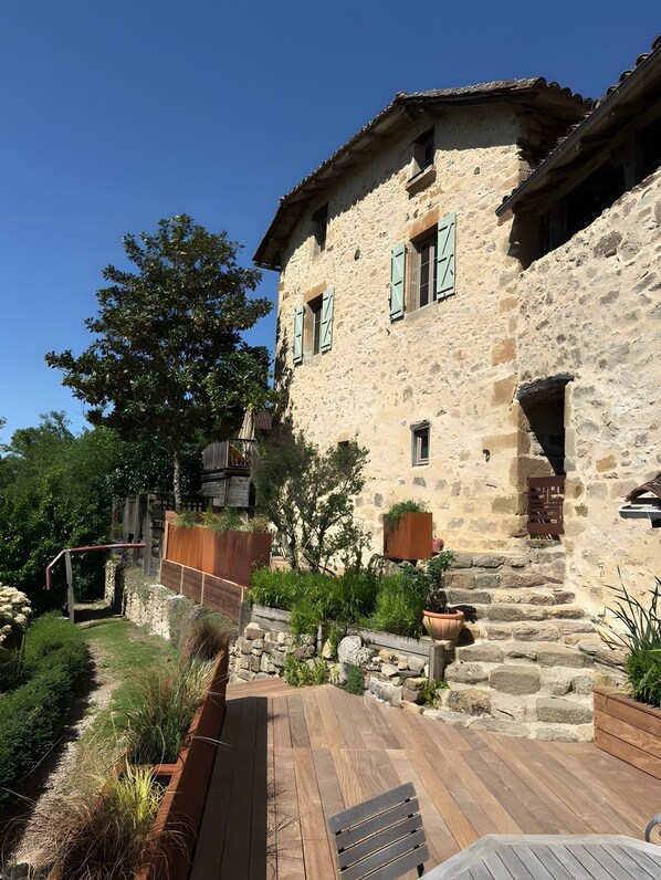 A stone building with a wooden deck, a stone wall, and a tree.