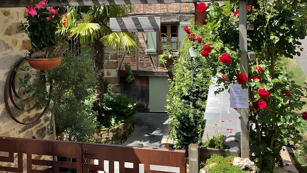 Un edificio de piedra con techo de tejas, una verja de madera y un rosal.
