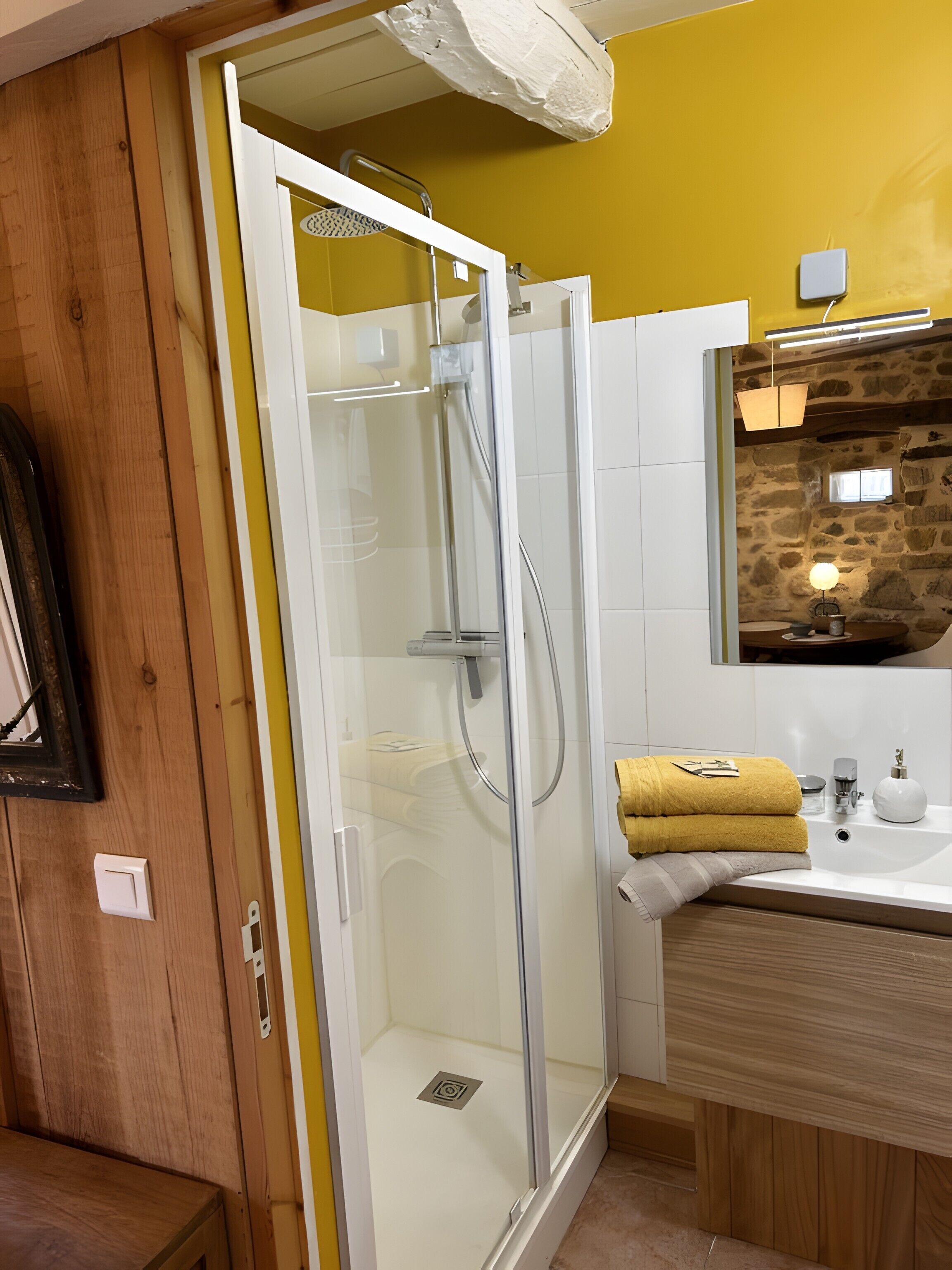 Un bagno con doccia vetrata, lavandino bianco e parete in pietra.