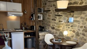 Una cocina rústica con paredes de piedra, una mesa de madera con sillas y un refrigerador pequeño.
