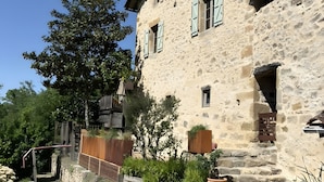 A stone building with a wooden deck, a stone wall, and a tree.