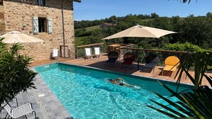 A swimming pool with lounge chairs and umbrellas, surrounded by stone buildings and greenery. - Cachou Guest Room with Shared Pool, Private Terrace and Wi-Fi (Felzins)