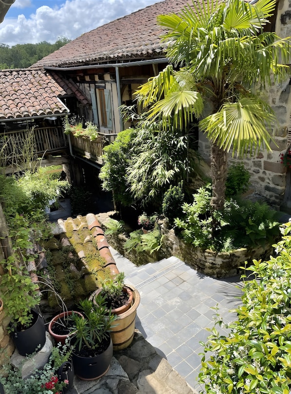 A courtyard with a stone wall, potted plants, and a tiled roof.