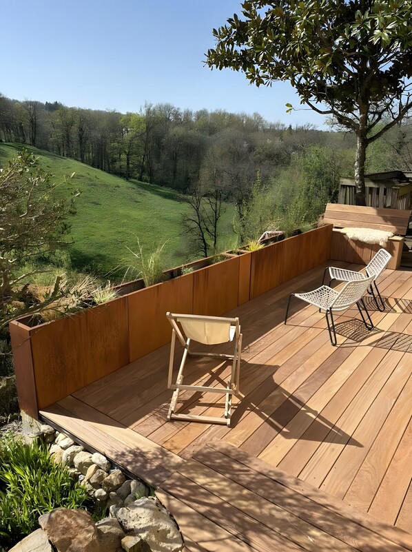 A wooden deck with a bench and two chairs, overlooking a grassy landscape.