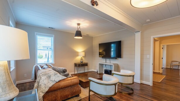 Una sala de estar moderna con un sofá de cuero marrón, dos sillones blancos, un televisor de pantalla plana montado en la pared y piso de madera.