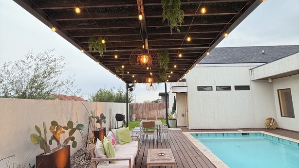 Eine Holzterrasse mit Pool, Sitzgelegenheiten im Freien und hängenden Pflanzen.